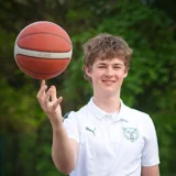 Sam Kousek v bílé klubové polokošili Wolves Radotín drží basketbalový míč